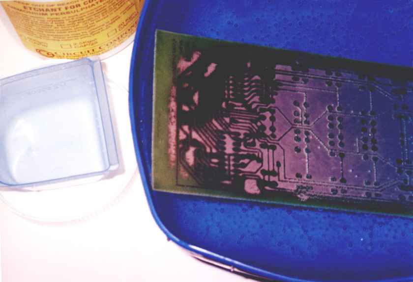 Keypad etching in persulphate. Pink areas of bare copper are being eaten away; darker areas protected by photoresist will remain. Note bubbles on board.